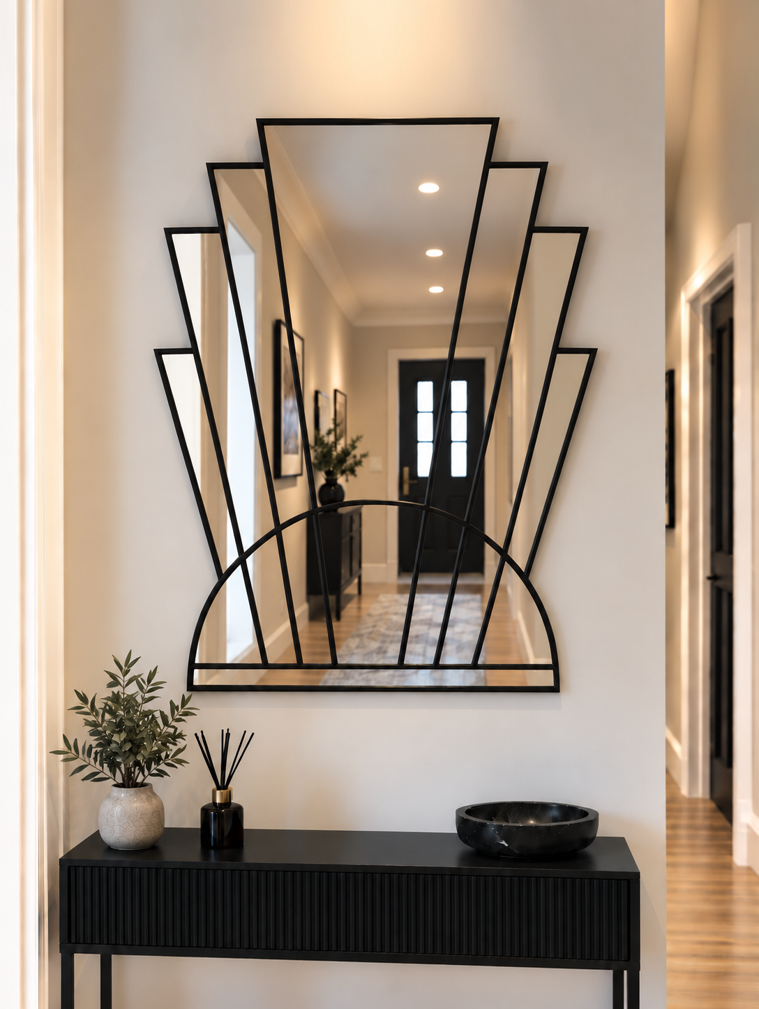 An Art Deco style wall mirror with a black metal frame, featuring vertical mirror panels and a semi-circular arch base, mounted on a white wall.