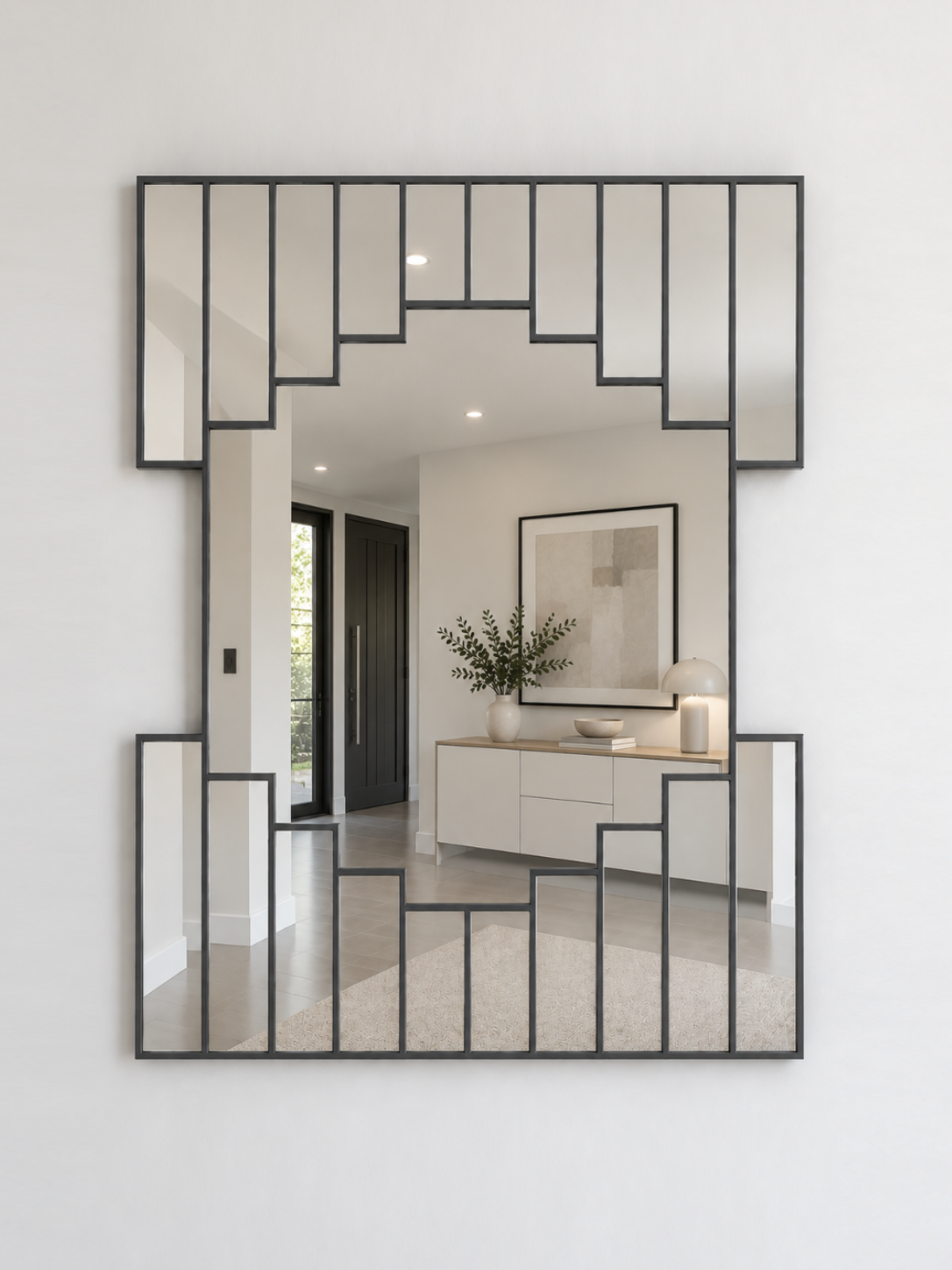 A large rectangular wall mirror with a antique geometric metal frame, mounted on a white wall. 