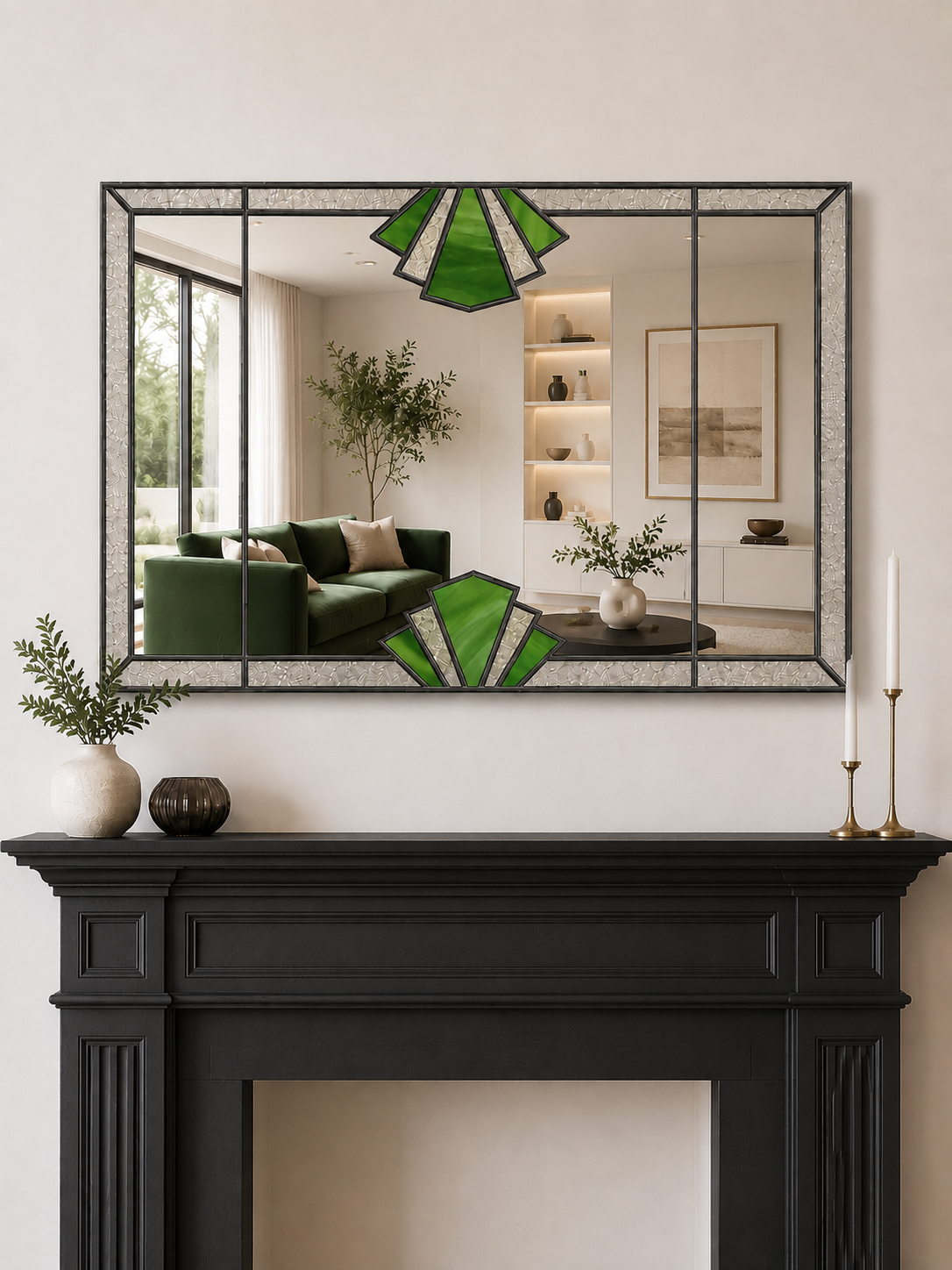 A rectangular wall mirror with a black metal frame and green-and-white fan-shaped stained-glass style accents, mounted above a black fireplace mantel in a styled interior.