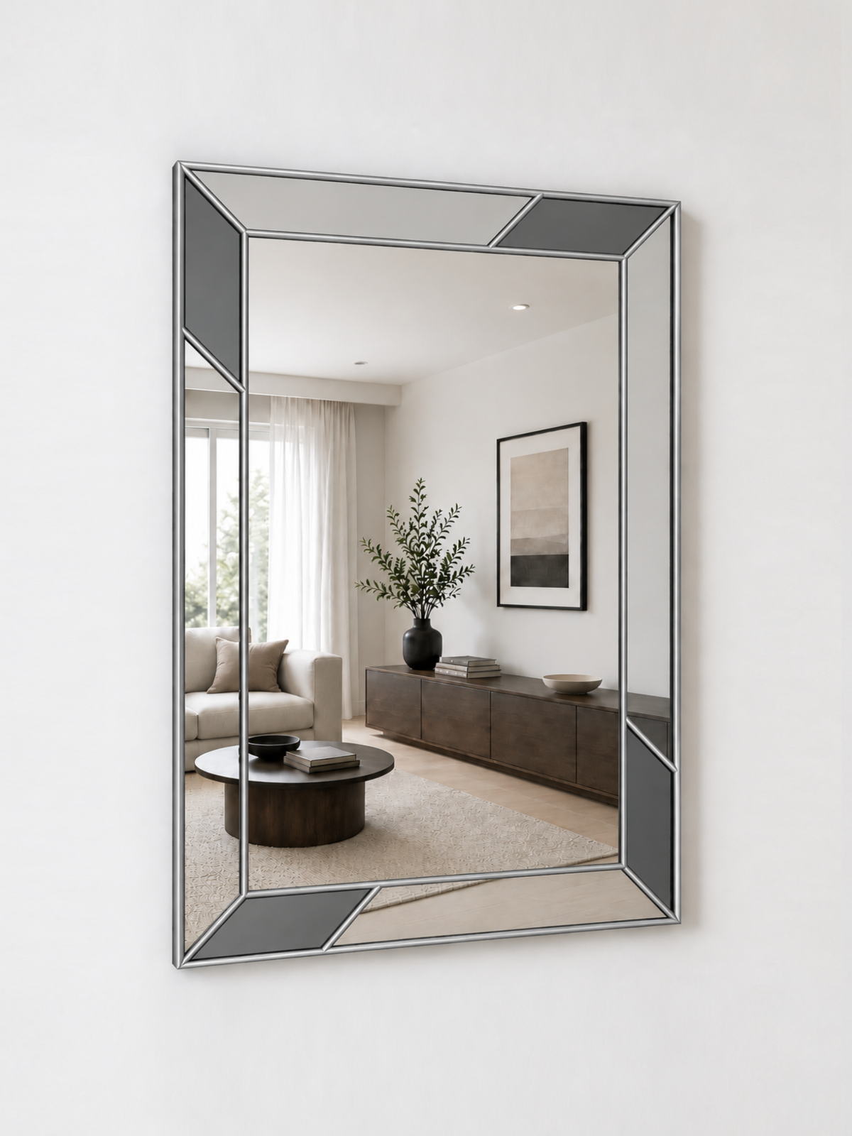 A geometric wall mirror with a silver metal frame and dark gray inset panels, mounted on a white wall.
