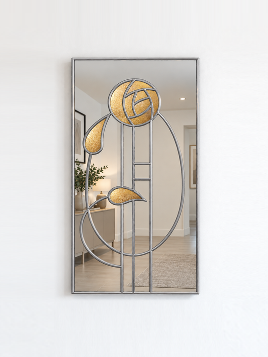 A vertical rectangular wall mirror with a silver Art Deco style frame featuring a stylized rose and leaf motif, mounted on a white wall.