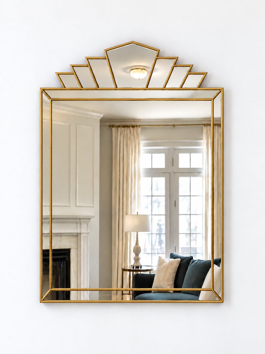 A rectangular wall mirror with a brass metal frame and a decorative geometric fan-shaped top, shown mounted on a white wall.